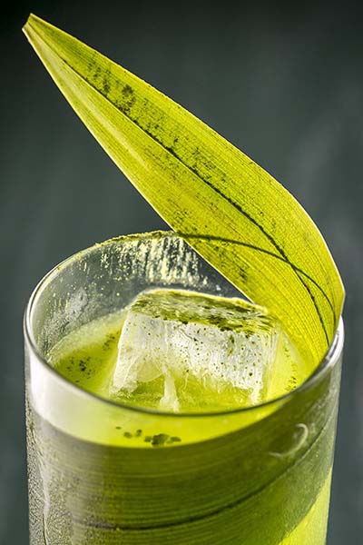 Closeup of a cocktail wrapped with a leaf and sprinkled with matcha.