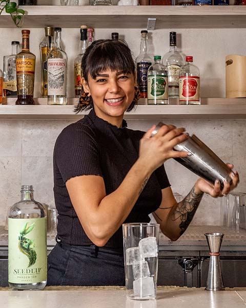 An adorable bartender laughing and smiling while shaking a cocktail photographed for the non-alcoholic spirit Seedlip.