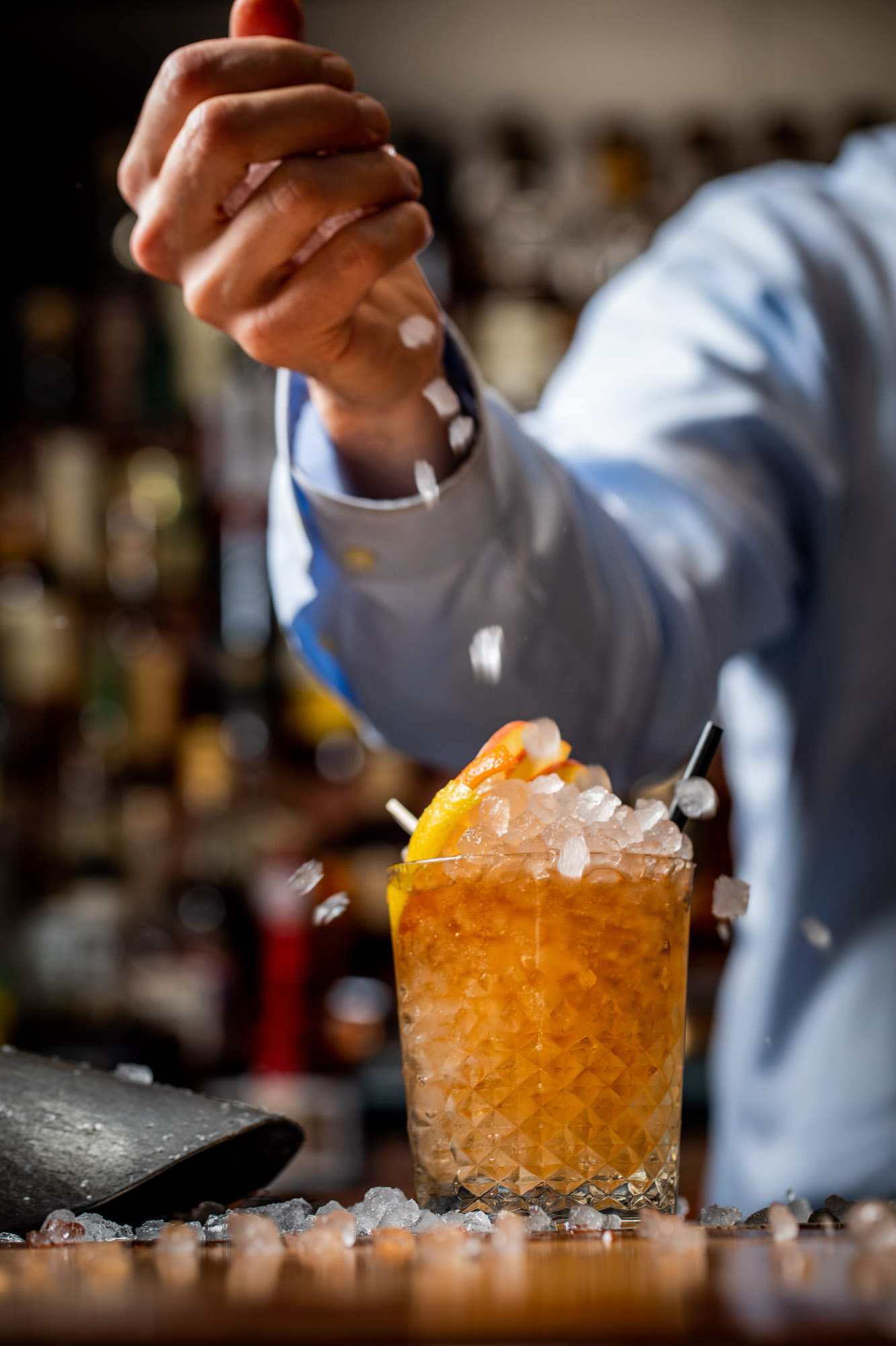 A hand dropping ice on a cocktail